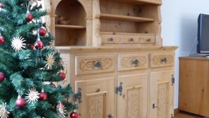 A wooden cabinet with multiple drawers and shelves, a small Christmas tree with ornaments, and a clock on the wall. - Chesa Thom / ÖV inklusive by Interhome (Pontresina)
