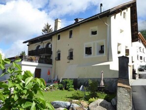 A two-story building with a balcony, a small garden with rocks and plants, and a clear sky. - Chesa Thom / ÖV inklusive by Interhome (Pontresina)
