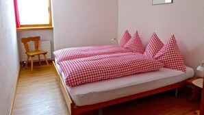 A bedroom with a wooden bed, checkered bedding, a chair, and a window. - Chesa Thom / ÖV inklusive by Interhome (Pontresina)
