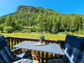 Une terrasse avec une table et des chaises, offrant une vue sur une montagne boisée.