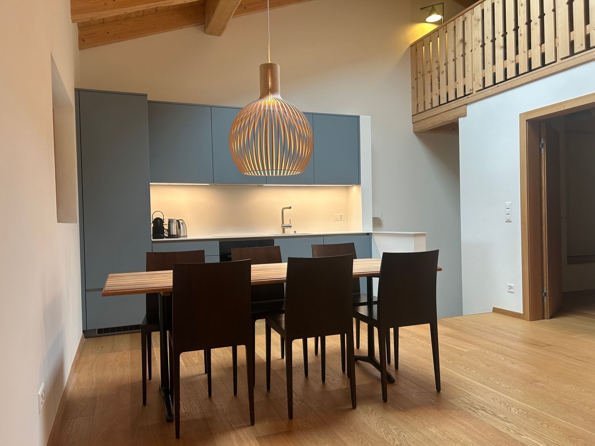A modern kitchen with blue cabinets, a wooden dining table, and a hanging pendant light.