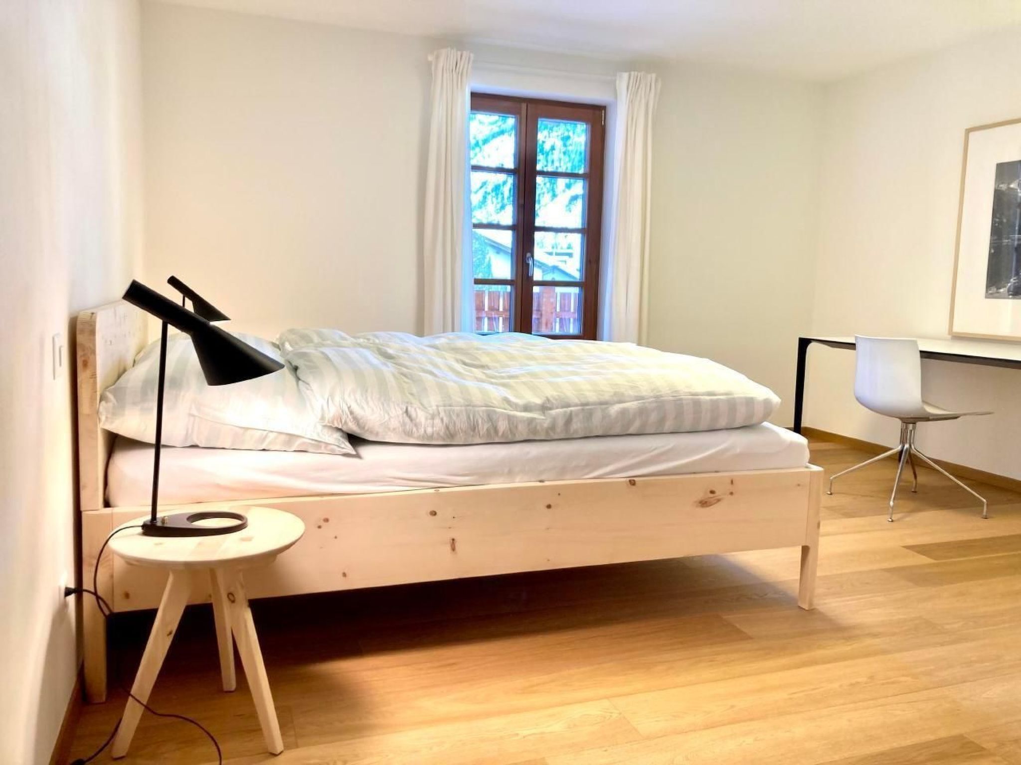 Un dormitorio con una cama de madera, una mesita de noche con una lámpara, una silla y una ventana con cortinas.