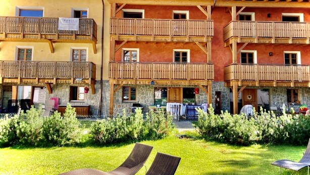Ein mehrstöckiges Hotel mit hölzernen Balkonen und einem gepflegten Gartenbereich mit Liegestühlen.