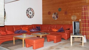 Una sala de estar con un sofá rojo, una mesa de centro de madera y un otoman. Hay un televisor sobre un mueble de madera.