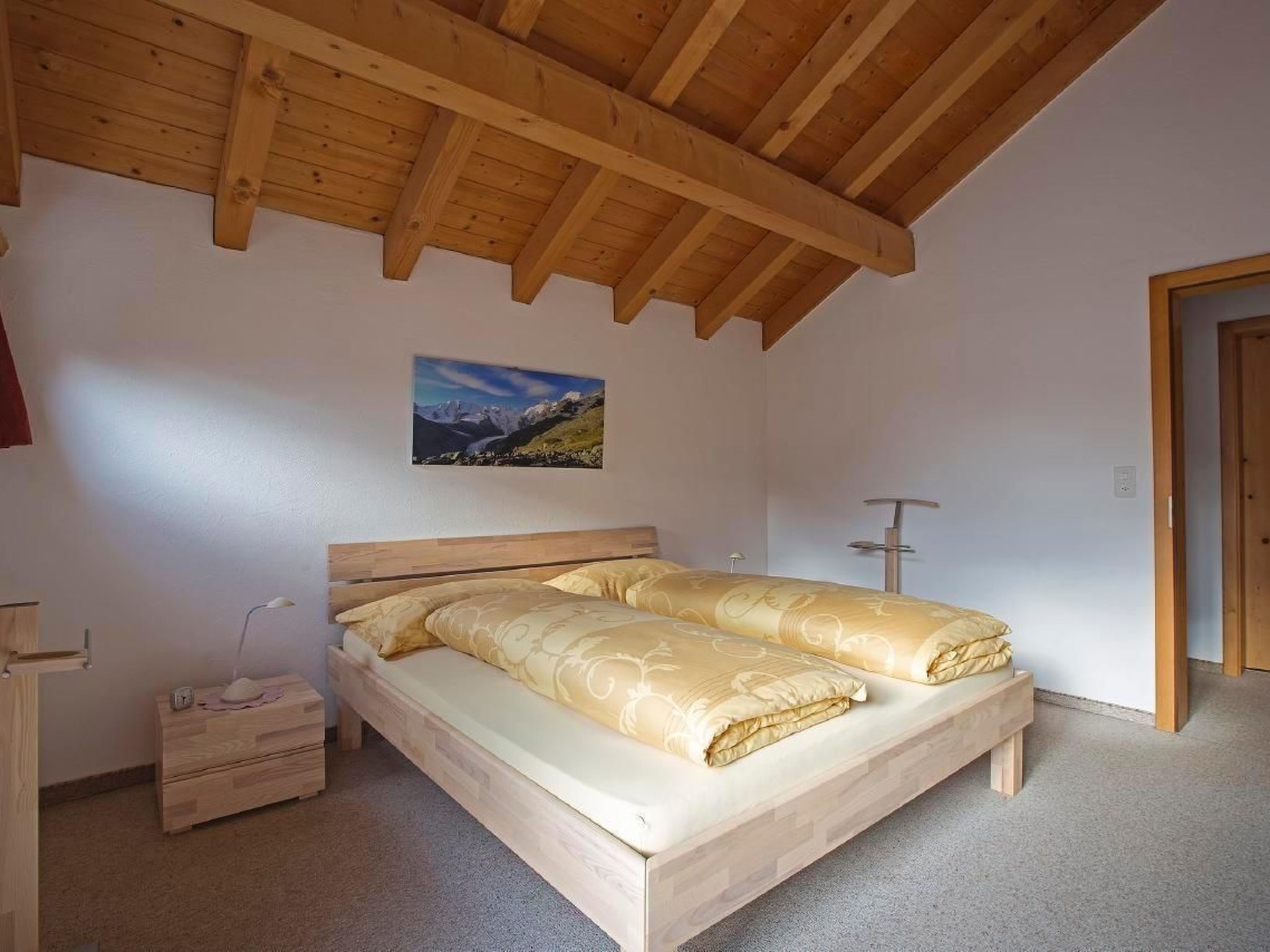 Un dormitorio con cama de madera, una mesita de noche, una lámpara y un cuadro en la pared.