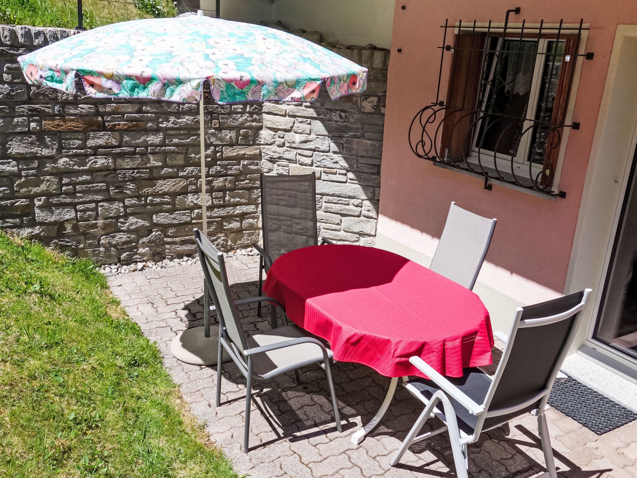 Eine Terrasse mit Tisch und Stühlen, einem gemusterten Sonnenschirm und einer Steinmauer.