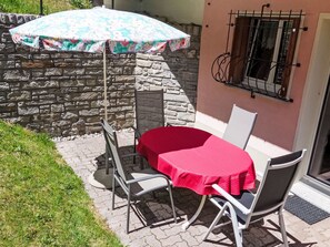 A patio with a table and chairs, a patterned umbrella, and a stone wall. - Chesa Suot God by Interhome (Pontresina)