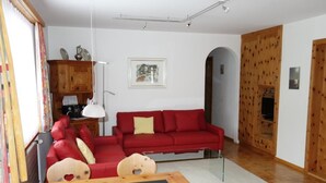 Ein Wohnzimmer mit einem roten Sofa, einem Holztisch, einer Lampe und einem Fernseher.
