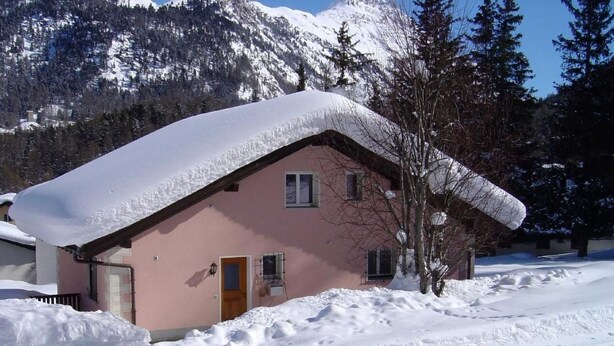 Ein mit Schnee bedecktes Haus mit geneigtem Dach, einer Holztür und Fenstern.