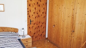 Ein Schlafzimmer mit Bett, Nachttisch, Lampe, Holzschrank und einer Tür.