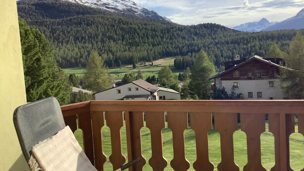 Een balkon met uitzicht op een berg, bos en huizen.