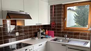 Een moderne keuken met witte kasten, een roestvrijstalen afzuigkap, een inbouwoven, een spoelbak en een raam met uitzicht op bomen.