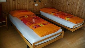 Deux lits superposés en bois, avec une literie orange, dans une pièce aux murs en bois et ornée d’un tableau encadré.