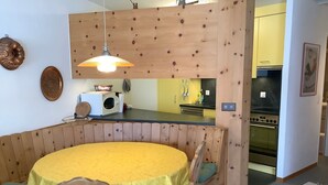 Eine kleine Küche mit integriertem Backofen und Mikrowelle, einer Wand in Holzoptik und einem gelben Esstisch mit Stühlen.