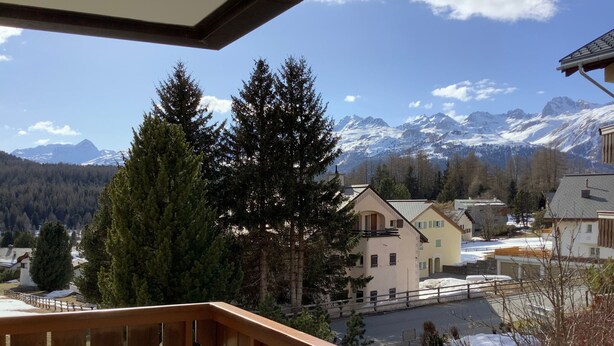 Ein Wohngebiet mit Blick auf schneebedeckte Berge, einem hölzernen Balkon und Häusern im traditionellen Baustil.