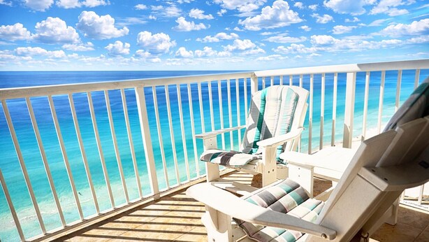 Uma varanda com vista para o oceano, uma cadeira branca e um deck de madeira.