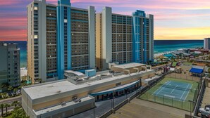 Um hotel com vários edifícios altos, uma quadra de tênis e vista para o oceano.