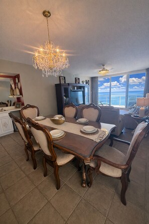 A dining area with a wooden table and chairs, a chandelier, and a view of the ocean. - Oceanfront 3BR 2 King Masters  Sleeps 7 (Panama City Beach)