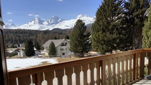 Ein Balkon mit Blick auf schneebedeckte Berge, einem Holzzaun und ein Gebäude mit einem geneigten Dach.