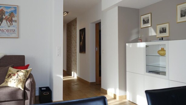 A modern living room with a sofa, a dining area with a white cabinet, and a hallway leading to another room. - Chesa Muragls by Interhome (Pontresina)