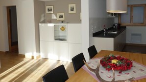 A modern kitchen with white cabinets, a dining table with a centerpiece, and a pendant light. - Chesa Muragls by Interhome (Pontresina)