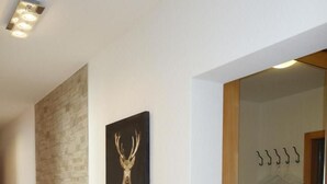 A hallway with a wooden floor, a stone wall, and a framed deer painting. - Chesa Muragls by Interhome (Pontresina)