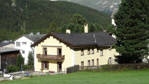 A two-story building with a balcony, surrounded by a grassy area and a wooden fence, with mountains in the background. - Chesa Kober; Giarsun by Interhome (Pontresina)