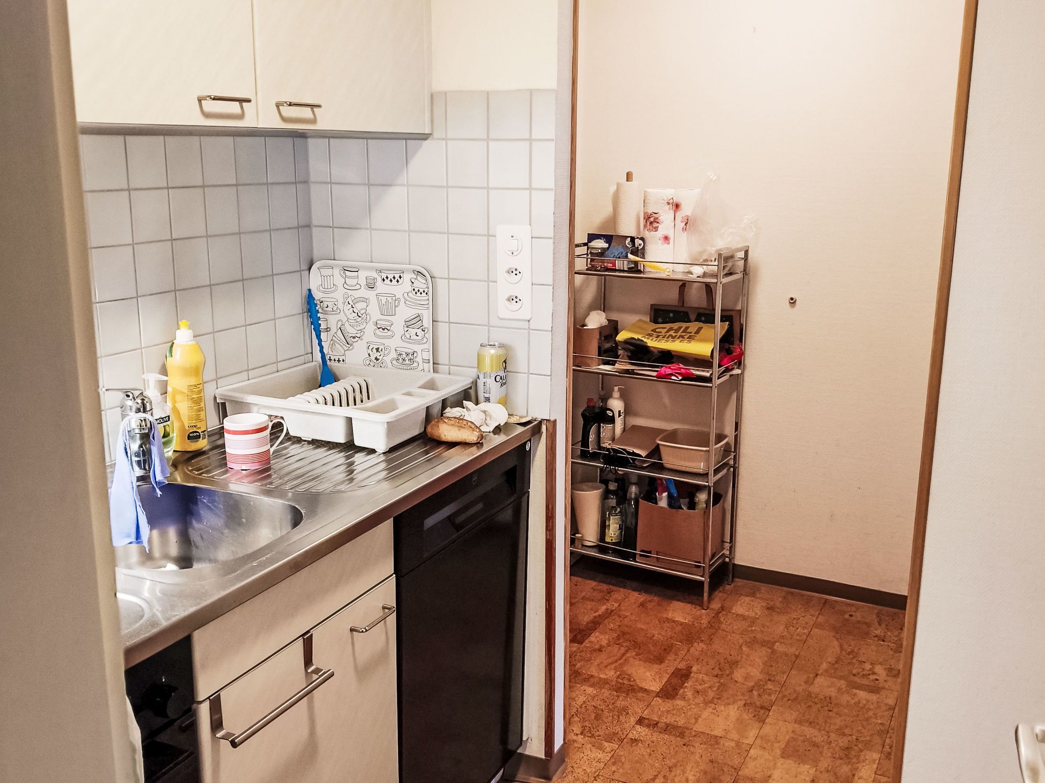 Cocina compacta con lavavajillas, pileta, protector de pared estampado y un mueble de metal con estantes.