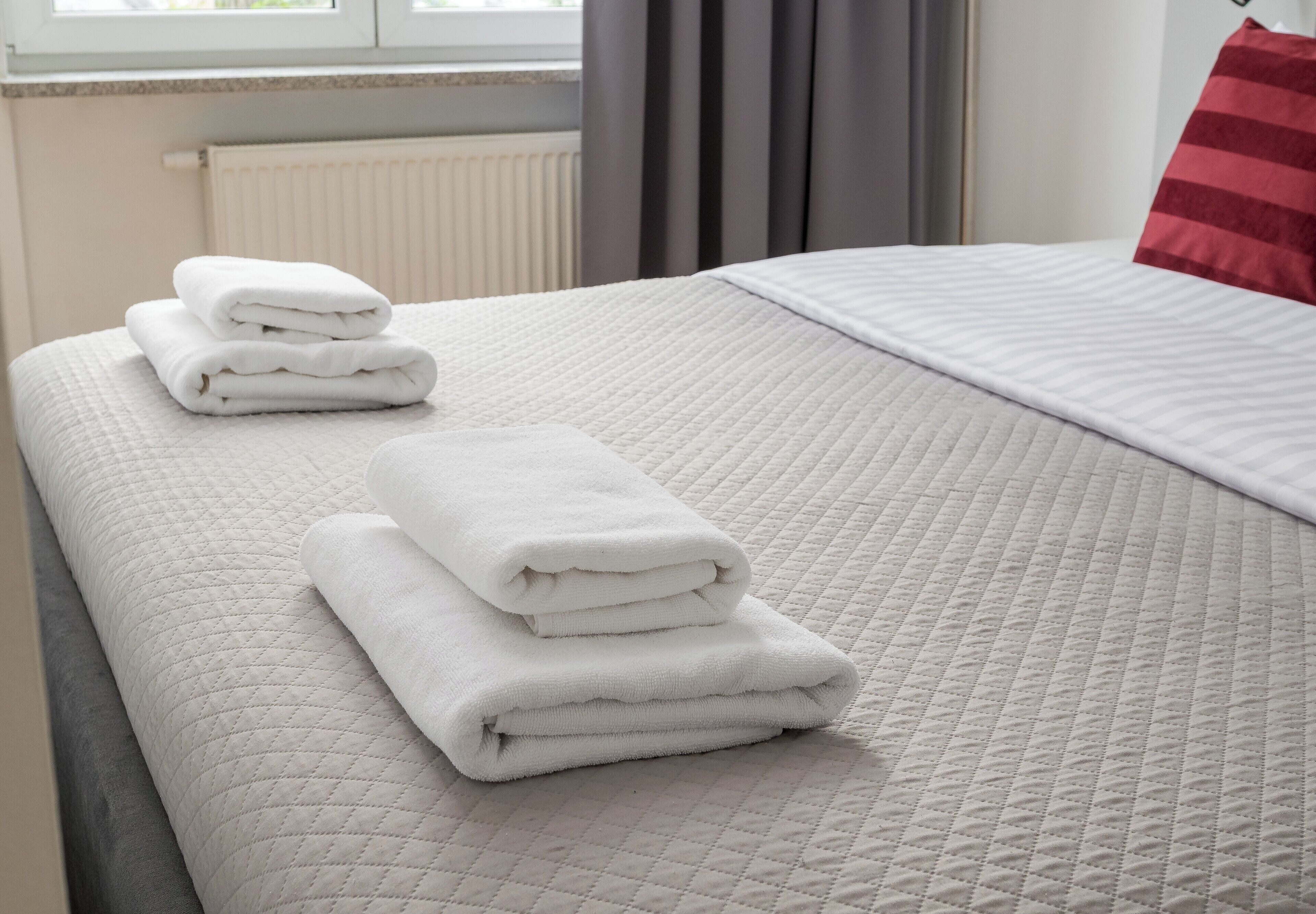 Una cama bien hecha con una colcha blanca acolchada y toallas blancas dobladas.