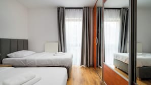 A hotel room with two beds, a wooden floor, a large mirror, and grey curtains. - Bemowo 2-Bedroom Apartment (Warszawa)