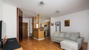 A modern living room with a grey sofa, wooden flooring, and a kitchen in the background. - Bemowo 2-Bedroom Apartment (Warszawa)