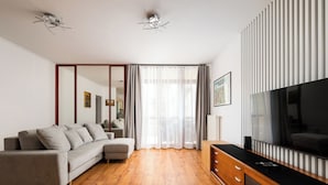 A modern living room with a sofa, wooden flooring, a TV, and a large mirror. - Bemowo 2-Bedroom Apartment (Warszawa)