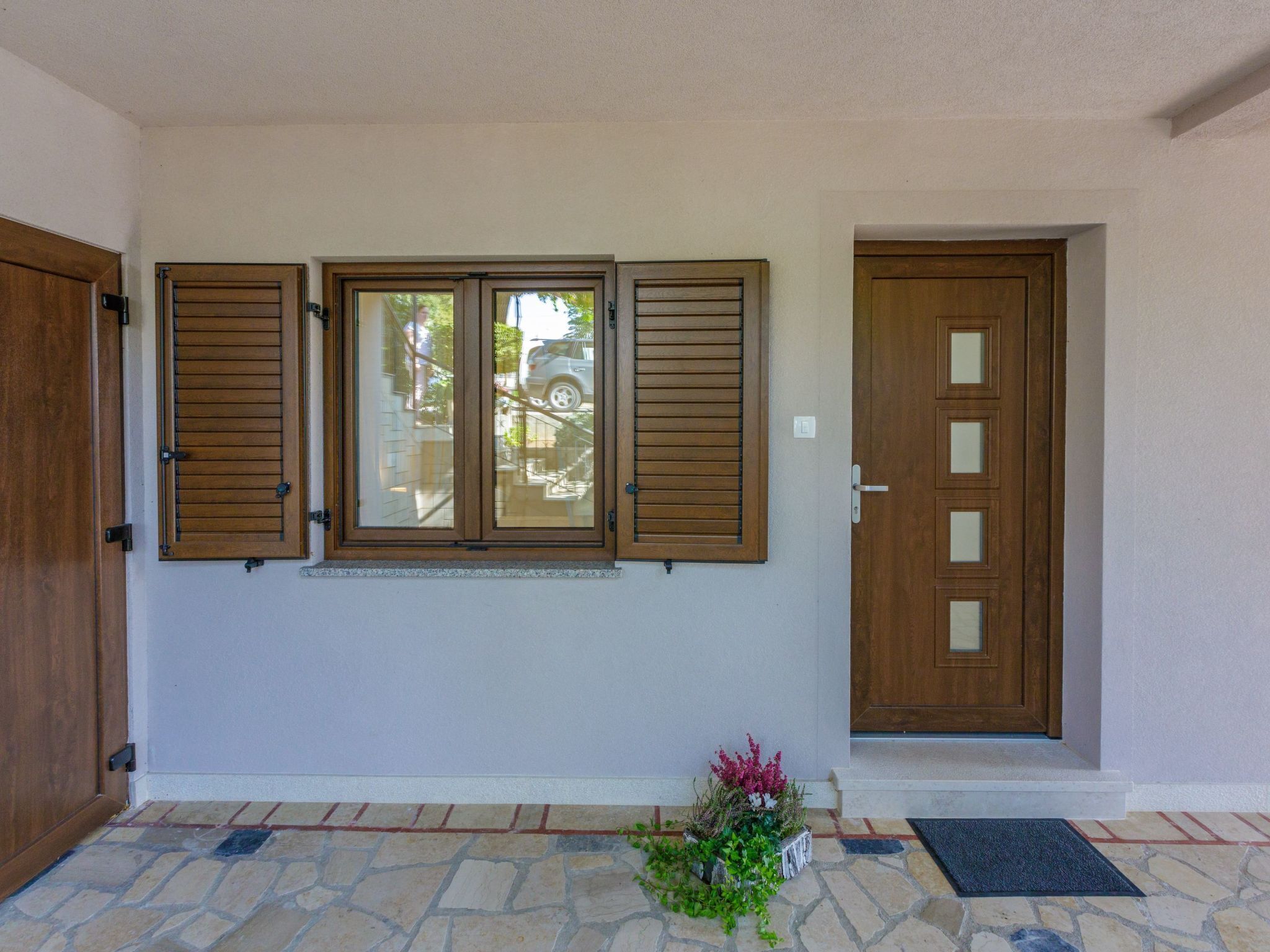 A front entrance with a stone-tiled porch, a wooden door, and a window with shutters.