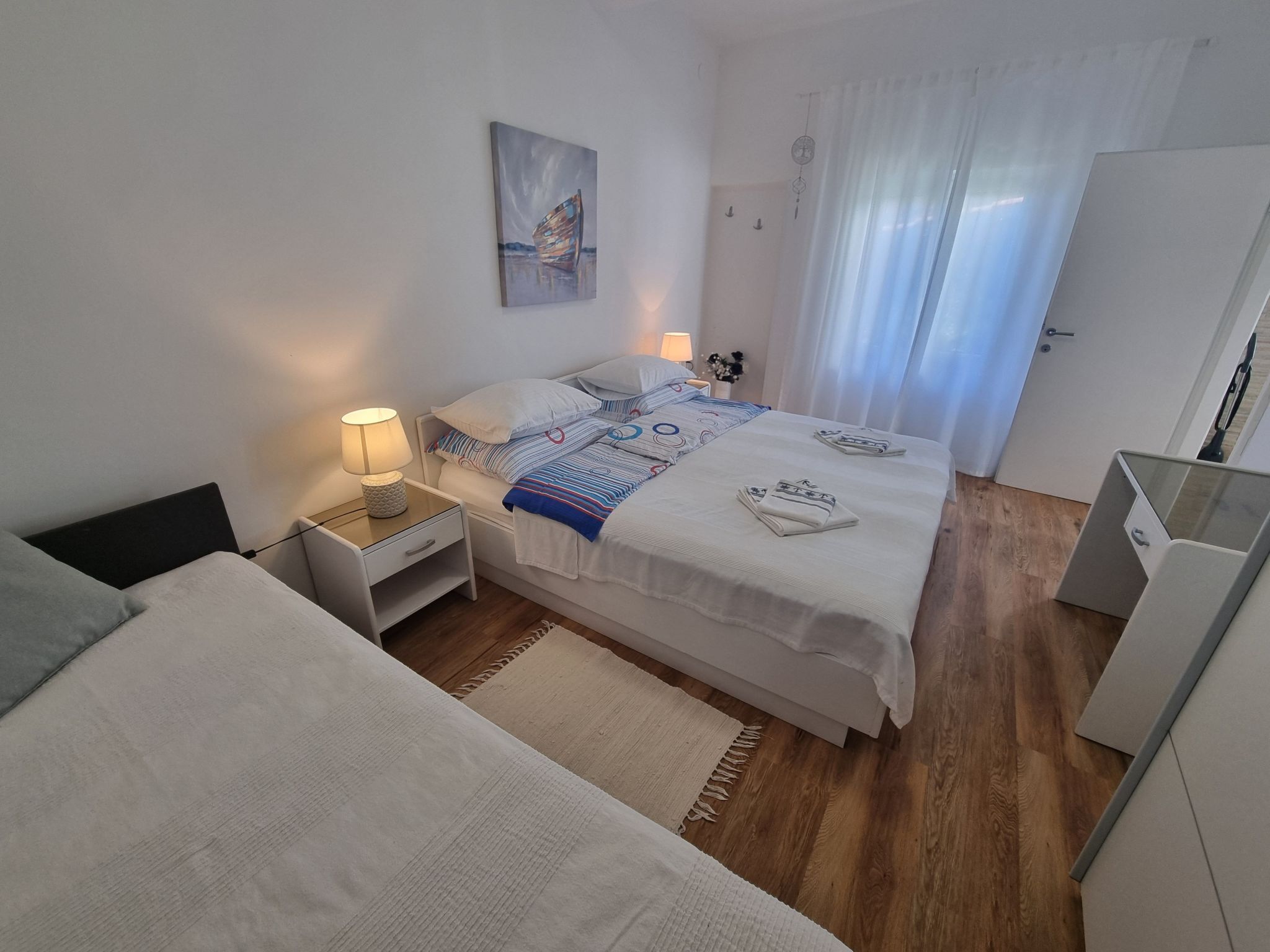 Een moderne slaapkamer met een bed, nachtkastjes, een schilderij en een raam met gordijnen.