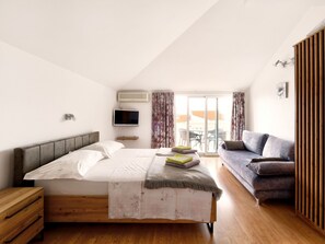 A modern bedroom with a large bed, a sofa, a TV, and a balcony with a view. - Studio-Apartment mit Balkon und Meerblick by Interhome (Crikvenica)