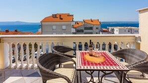 A balcony with wicker chairs and a table, overlooking a coastal view with buildings and the sea. - Studio-Apartment mit Balkon und Meerblick by Interhome (Crikvenica)