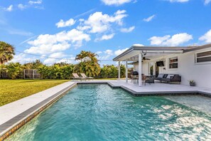 Une piscine avec un patio couvert, une pelouse et des palmiers.
