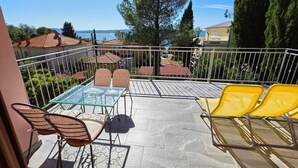 Eine Terrasse mit Tisch und Stühlen, Blick auf das Meer und umliegende Häuser.