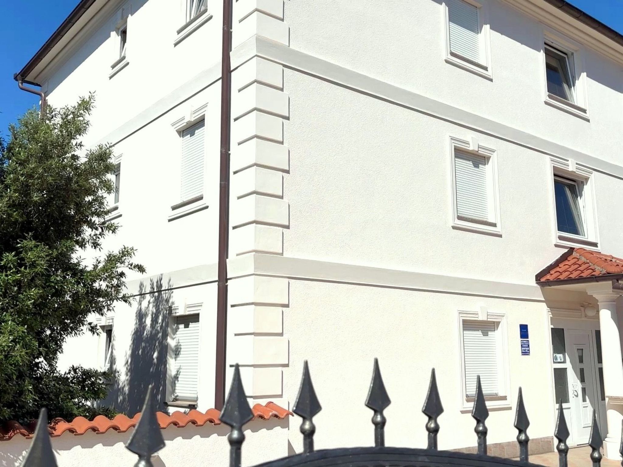 A white building with a tiled roof, multiple windows, and a metal fence with pointed tops.