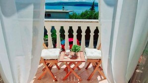 Un balcone con due sedie di legno, un tavolino, una pianta in vaso e vista sul mare e sul verde.