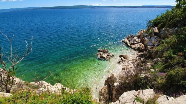 Paesaggio costiero con acque blu cristalline, rocce e vegetazione.