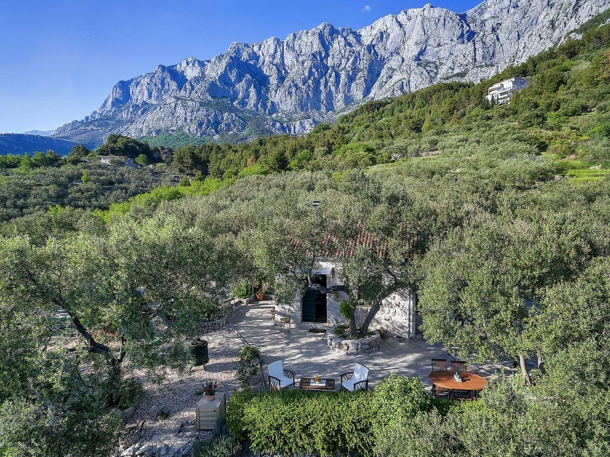 Ein abgelegener Sitzbereich im Freien mit Steintischen und -stühlen, umgeben von üppiger Vegetation mit Blick auf eine Berglandschaft.