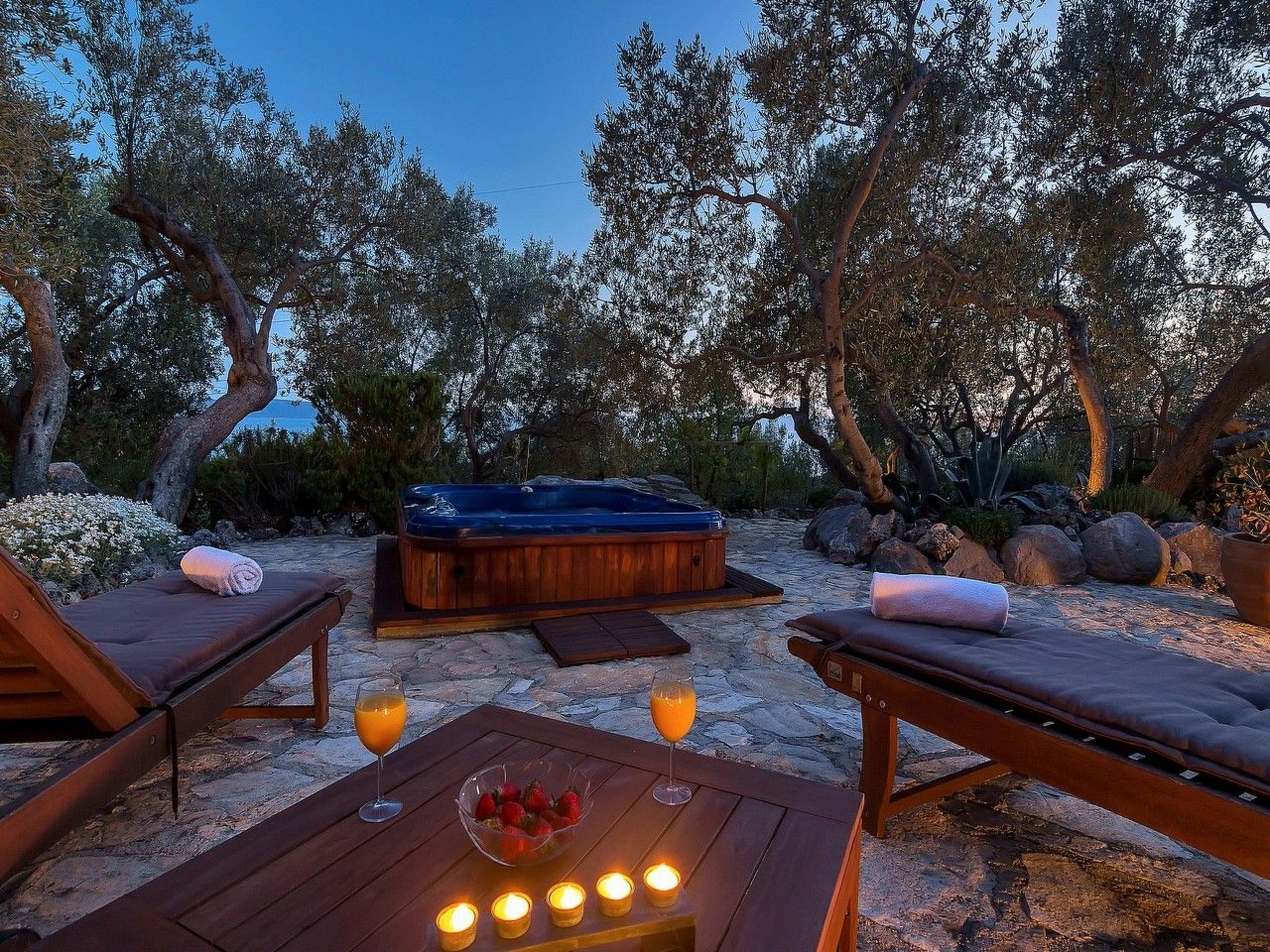 A serene outdoor setting with a hot tub, lounge chairs, and a table with candles and fruit.