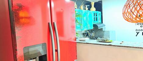 A kitchen with a red refrigerator, teal cabinets, and a decorative orange light fixture.