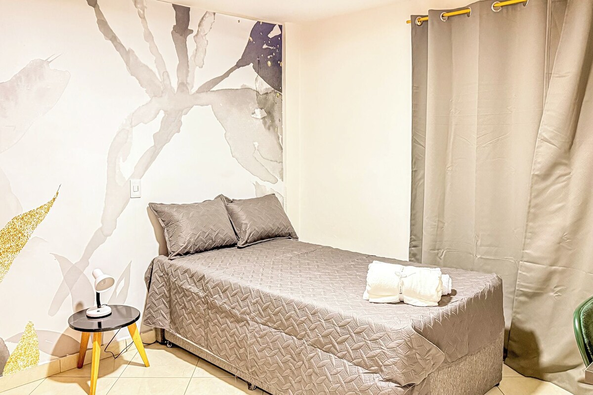A bedroom with a bed, a small table, a chair, and a curtain.