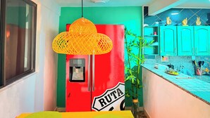 Une cuisine avec un réfrigérateur rouge, un luminaire suspendu jaune et une plante en bambou.