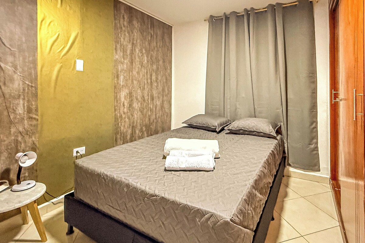 A bedroom with a bed, pillows, a bedside table, and a door.
