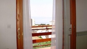 Ein Zimmer mit Holzbalkon, weißen Vorhängen und Blick auf Gebäude und Grünflächen.
