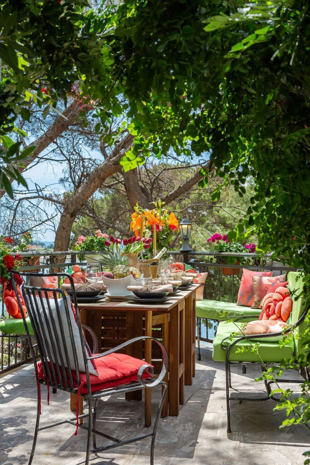 An outdoor dining area with a wooden table set for four, surrounded by chairs with red cushions.