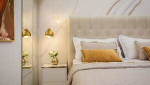 Quarto com cabeceira estofada, mesa de cabeceira com um vaso de flores e duas luminárias fixadas na parede.